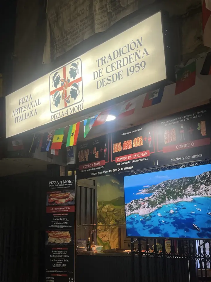 Local de Pizza 4 Mori con el aviso 'Tradición de Cerdeña desde 1959' y una pantalla con playas de Cerdeña