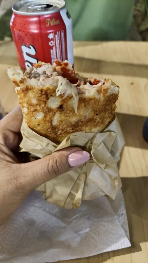 Porción de pizza envuelta en papel con una gaseosa